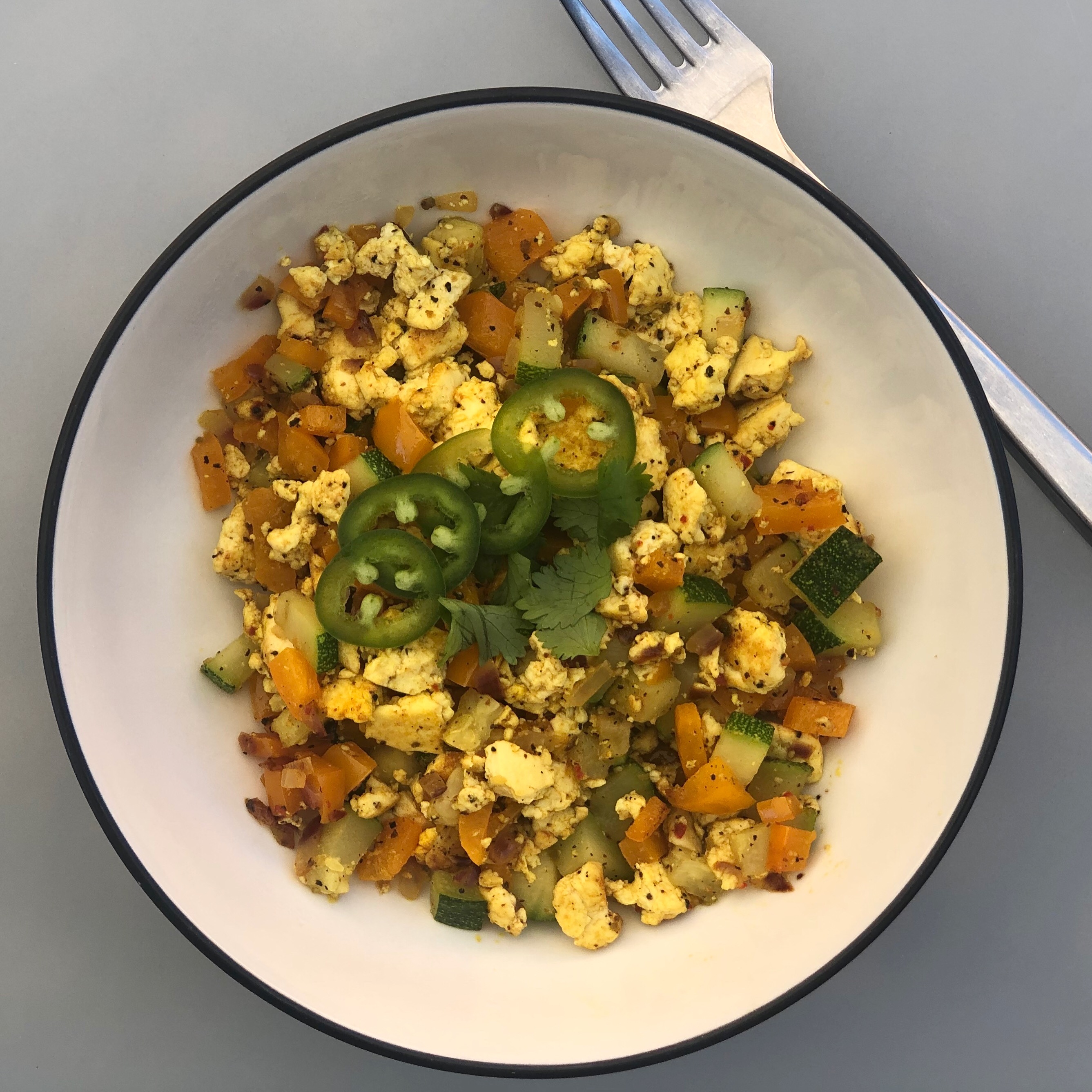 Photo of tofu scramble with vegetables and topped with cilantro and sliced jalapenos.