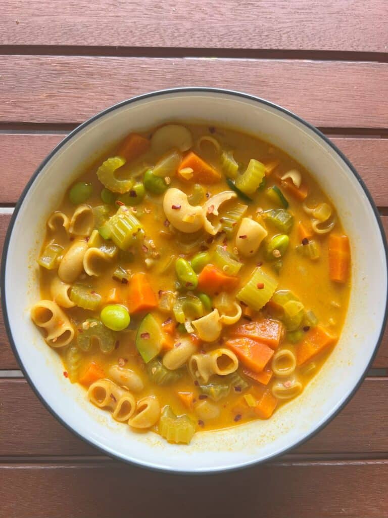 Bowl of coconut curry soup with vegetables and edamame. Soup is topped with red chili flakes.