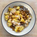 Bowl of roasted chickpeas and cauliflower seasoned with curry powder and topped with yogurt dressing.