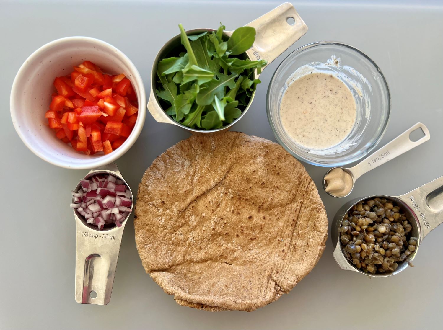 Ingredients in the Lentil Pita Wrap Recipe-whole wheat wrap, mustard, onion, bell pepper, arugula, lentils, and homemade yogurt dressing.