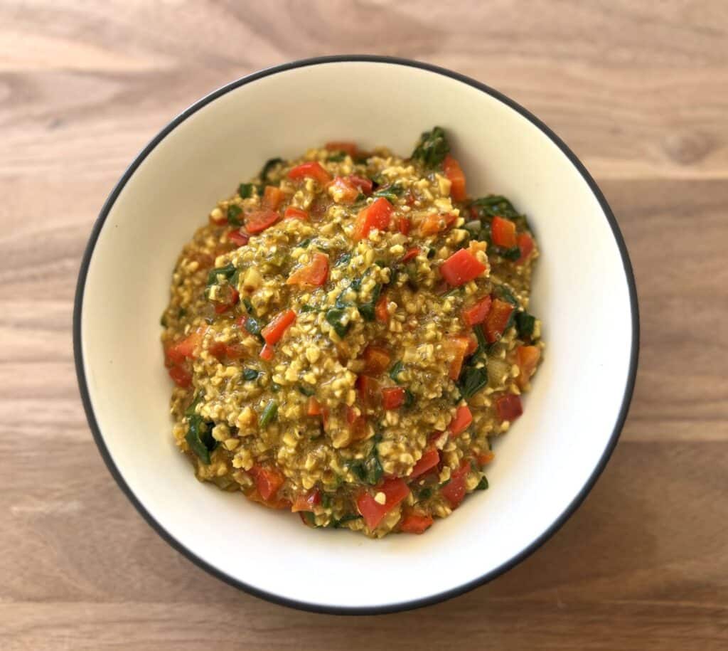 Bowl of savory vegetable oats with bell pepper, leafy greens, onion and seasonings.