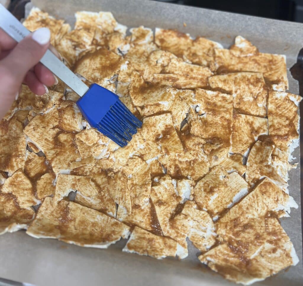 Thin tofu slices laid out on a baking sheet and being coated in the marinade for the vegan deli meat.