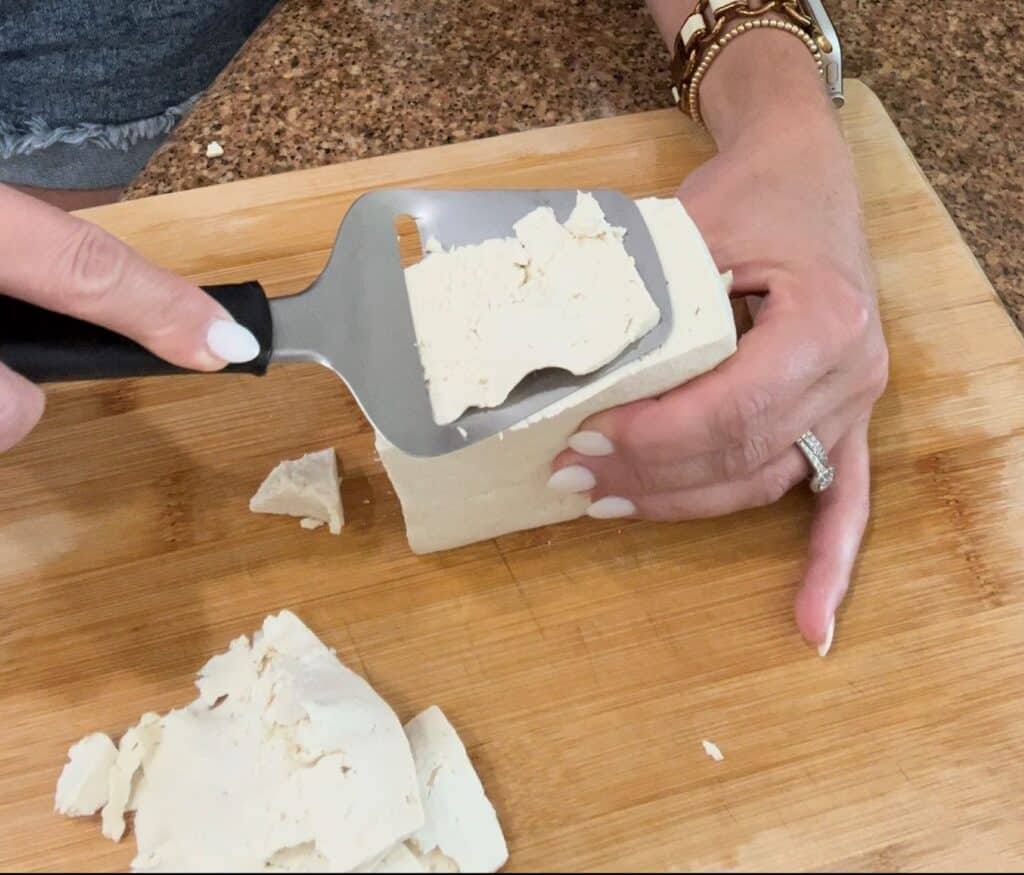 Cutting thin slices of a block of tofu to make vegan deli meat.