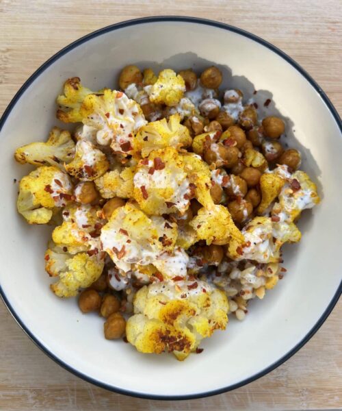 Bowl of roasted chickpeas and cauliflower seasoned with curry powder and topped with yogurt dressing.